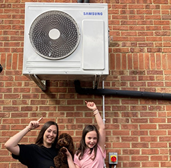 Woman, child and dog standing below heat pump