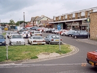 An image of a row of shops showing cars parked in the parking area in front of the shops.