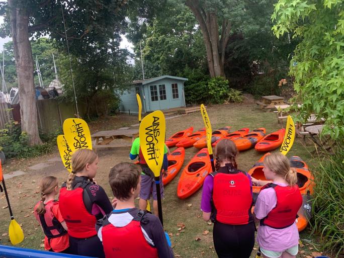 Photo of children holding paddles standing in front of kayaks