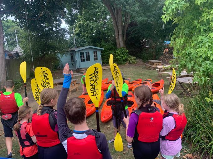 Photo of children holding paddles standing in front of kayaks